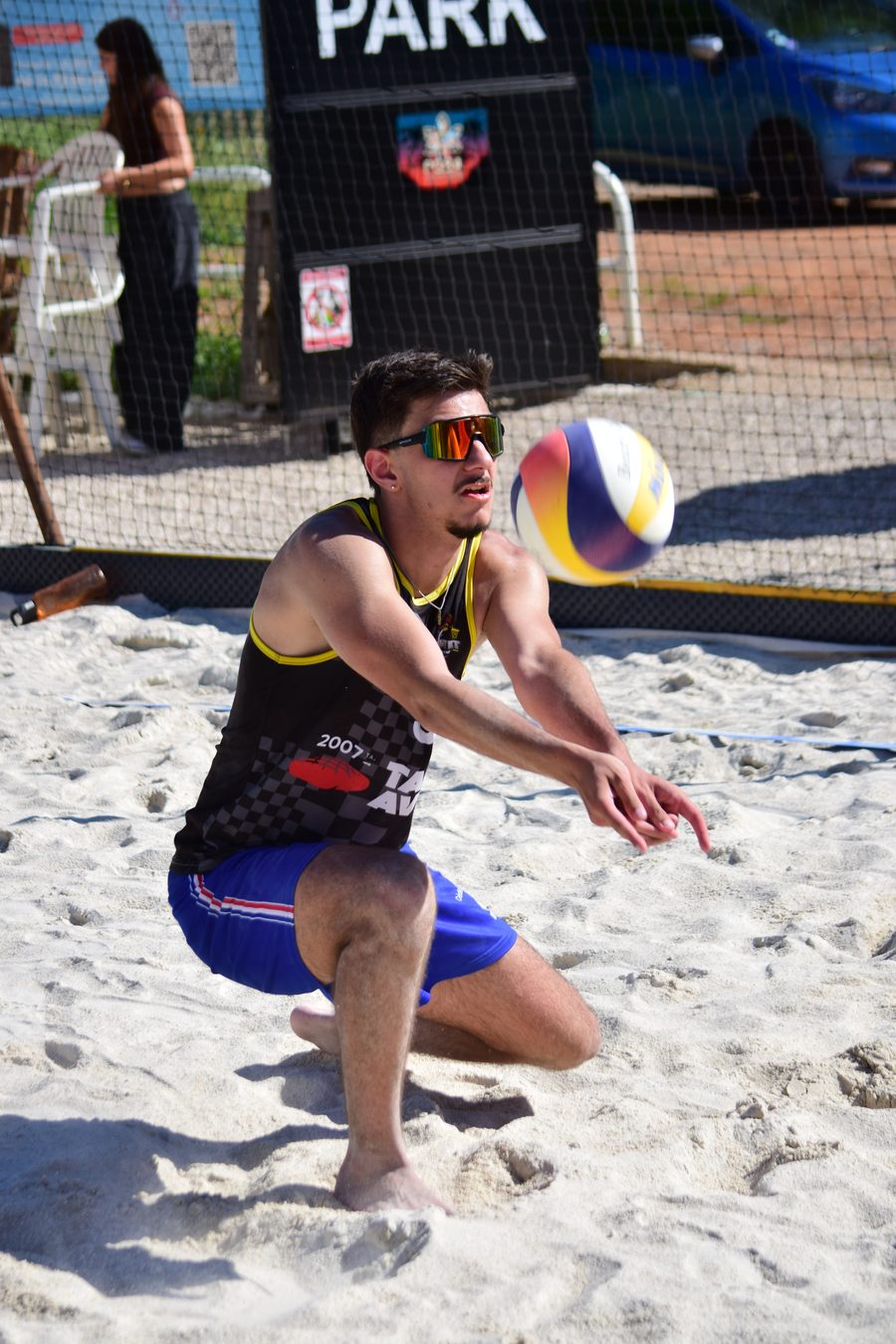 Joueur du club en maillot noir et or, un genou dans le sable, bras tendus pour réceptionner le ballon qui arrive sur sa gauche