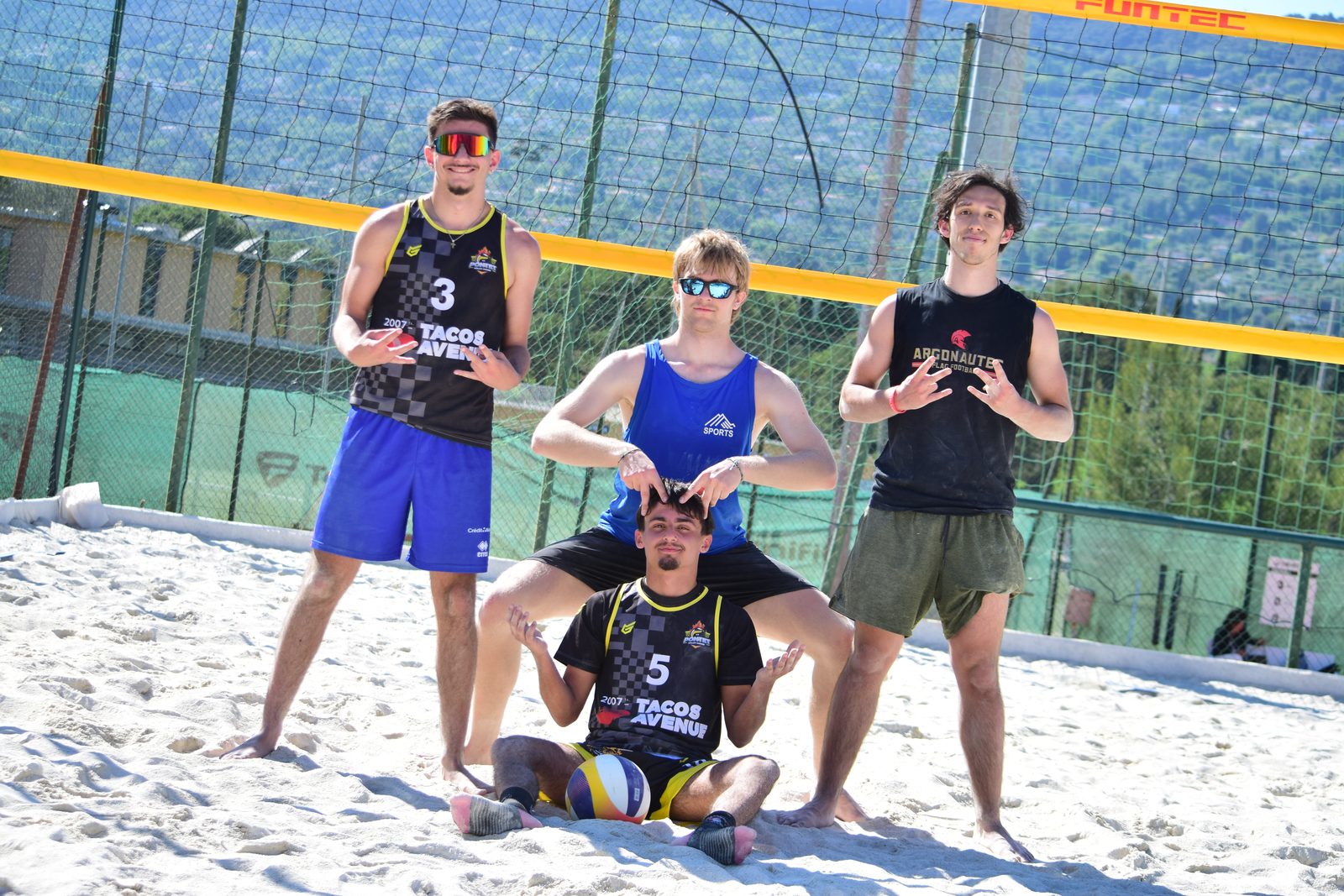 Quatre joueurs posent en souriant sur un terrain de sable, dont deux en maillot noir et or du Pontet floqués 3 et 5, collines boisées en arrière-plan