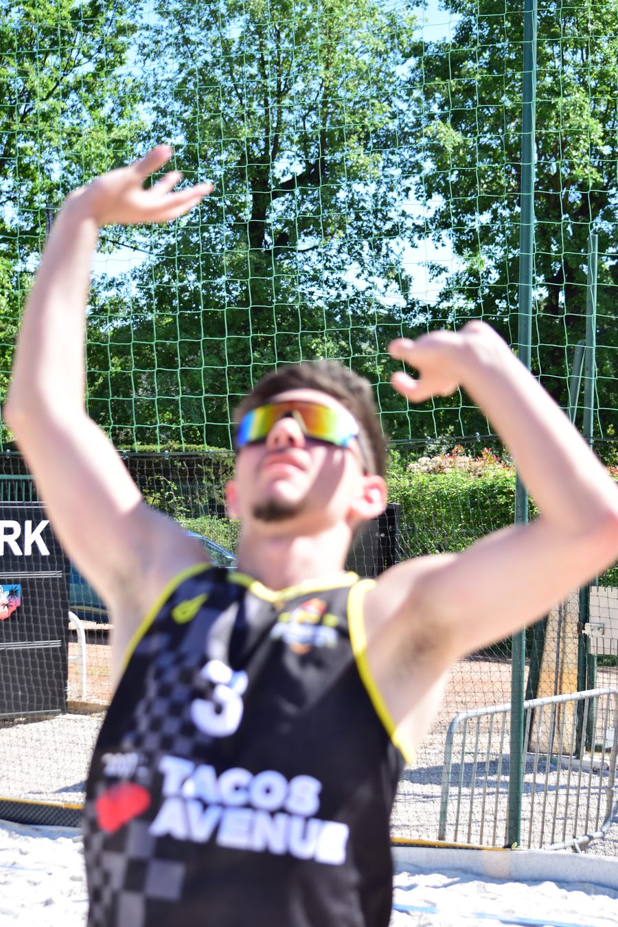 Joueur du club en maillot noir et or, lunettes de soleil, mains au-dessus de la tête au moment de la passe